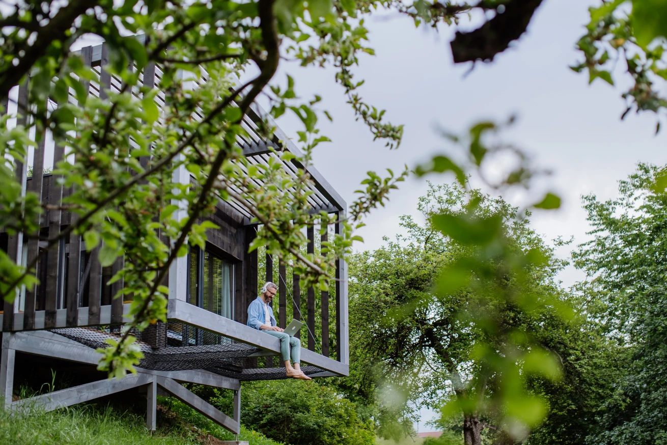 Männliche Person mit Laptop im modernen Baumhaus